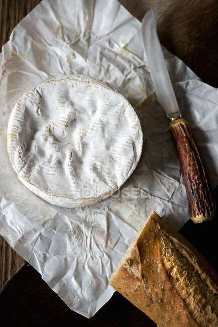 Queijo Camembert inteiro de cima em seu invólucro com faca de queijo e baguete — Fotografia de Stock