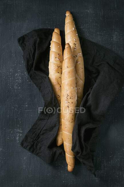 Три крученых хлеба с солью и тмином на черном текстиле — стоковое фото