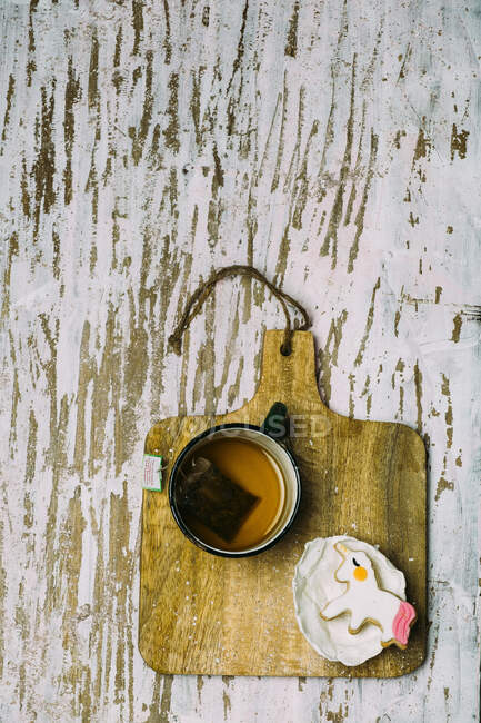 Unicorn cookie with a cup pf tea on a wooden plank on a white surface — Stock Photo