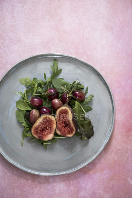 A salad with figs, garpes and lettuce on a grey plate on a pink backdrop — Stock Photo