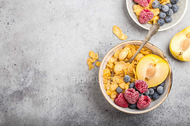 Cornflakes aux framboises glacées, bleuets et prunes jaunes dans des bols — Photo de stock