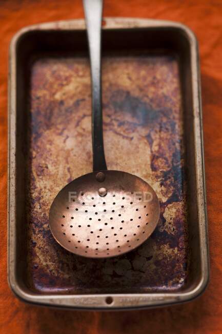 A burnt roasting tin with a strainer spoon — Stock Photo