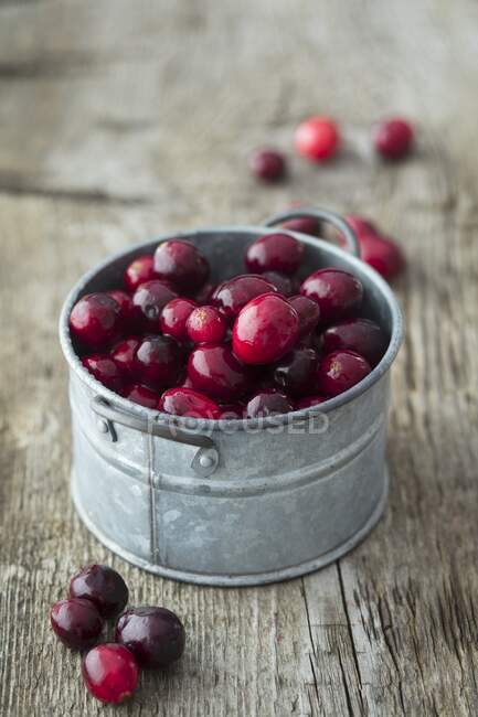 Cranberries em recipiente de metal e na superfície de madeira rústica — Fotografia de Stock
