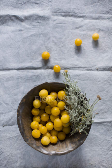 Mirabelle prunes dans un bol en bois avec des herbes et sur tissu gris — Photo de stock