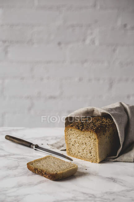 Slice load of bread wrapped in linen cloth on marble table with knife — Stock Photo