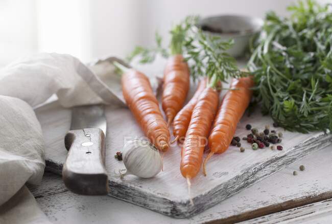Fresh carrots with garlic and pepper on chopping board — Stock Photo