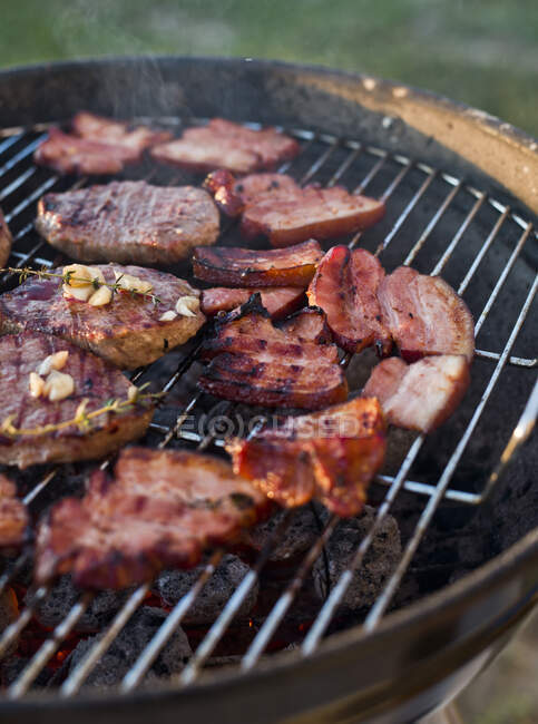 Beef steaks and bacon on a grill — Stock Photo