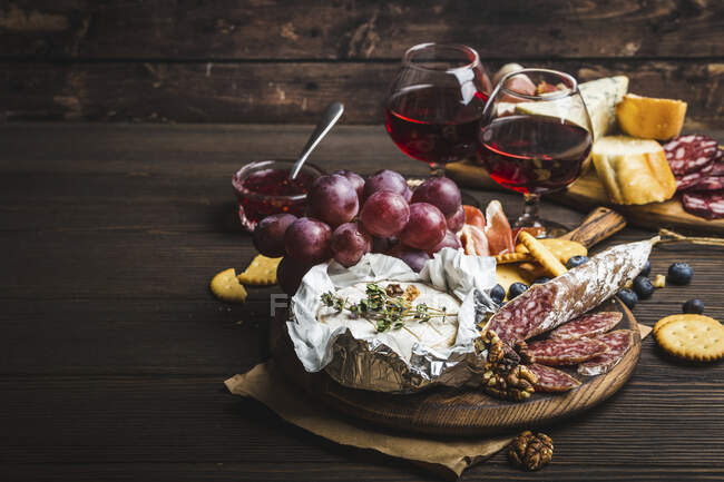 Un plateau de fromage, viande, craquelins, pain, raisins et noix avec du vin rouge — Photo de stock