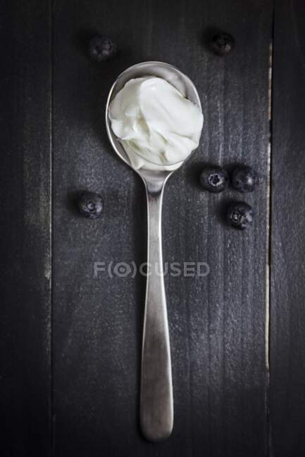 Yogurt on spoon with blueberries on wooden surface — Stock Photo