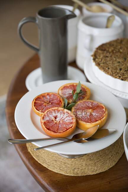Карамельные грейпфруты на тарелке с зелеными листьями и ложками на тарелке — стоковое фото