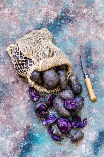 Pommes de terre violettes dans un sac et un couteau de nettoyage — Photo de stock