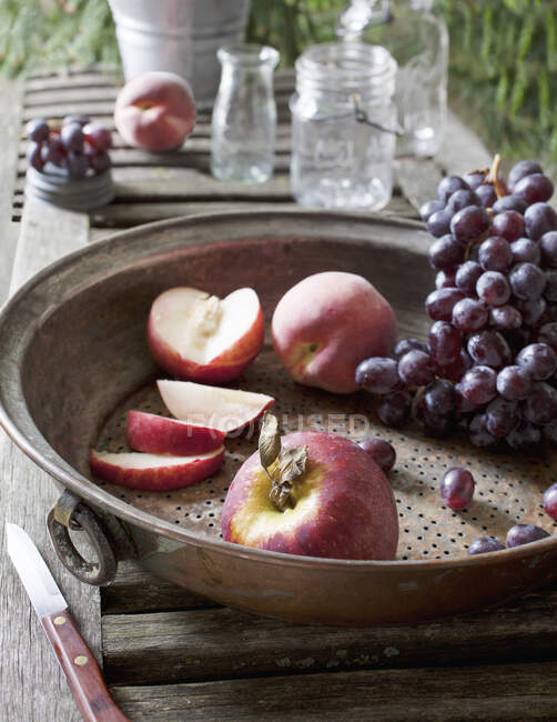 Setaccio metallico con uva e pesche intere e tagliate — Foto stock