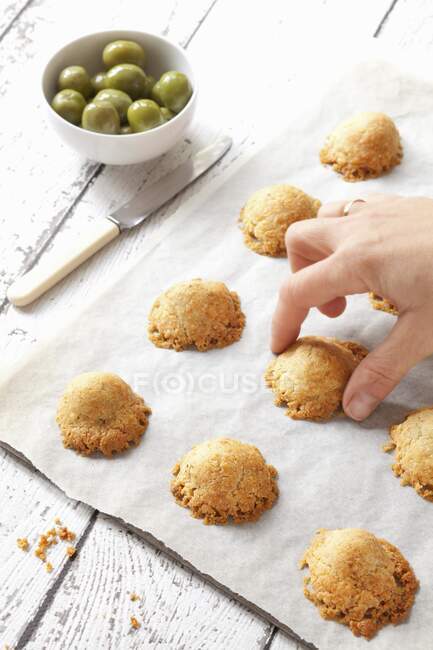 Hand picking cheese pastry from baking paper — Stock Photo