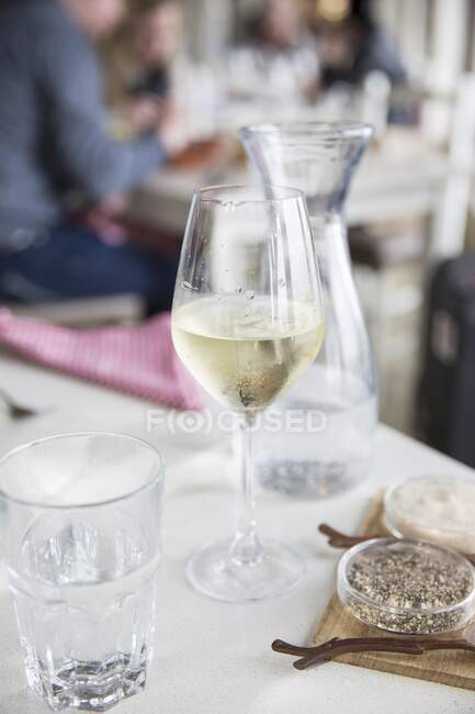 A glass of white wine with water, salt and pepper on a table in a restaurant — Foto stock