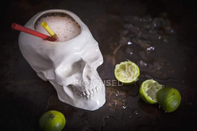 Zombie-Cocktail serviert in Totenkopf-Tasse mit Strohhalmen und gepressten Limetten auf Hintergrund — Stockfoto