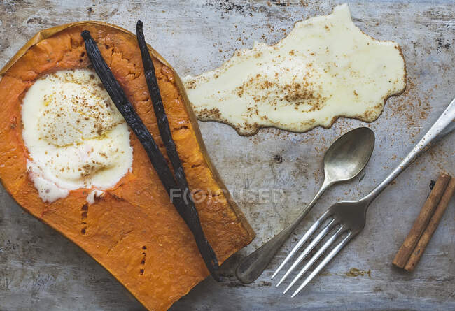 Backed pumpkin half with a scoop of vanilla ice-cream, vanilla sticks, cinnamon, a fork and a tea-spoon — Stock Photo