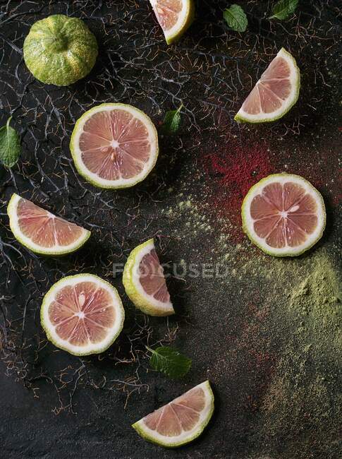 Sliced pink tiger lemon with mint leaves on branches with pink and green powder — Stock Photo