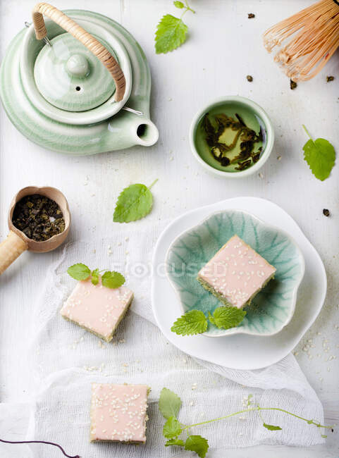 Matcha green tea cakes with white chocolate glaze and sesame seeds with a cup of green tea and balm, mint leaves. — Stock Photo