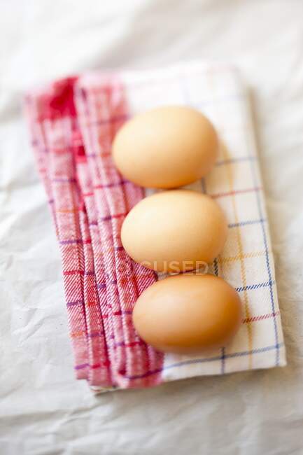 Fresh eggs on checkered tea towel — Stock Photo