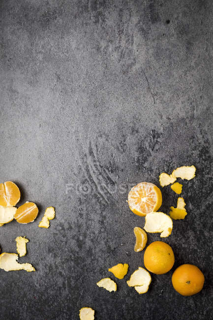 Цілі і очищені мандарини на поверхні чорного каменю — стокове фото