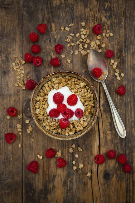 Granola with yoghurt and raspberries in bowl and on wooden table with spoon — Stock Photo