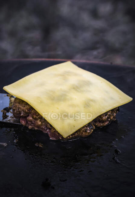A hamburger patty topped with cheese in a grill pan — Stock Photo