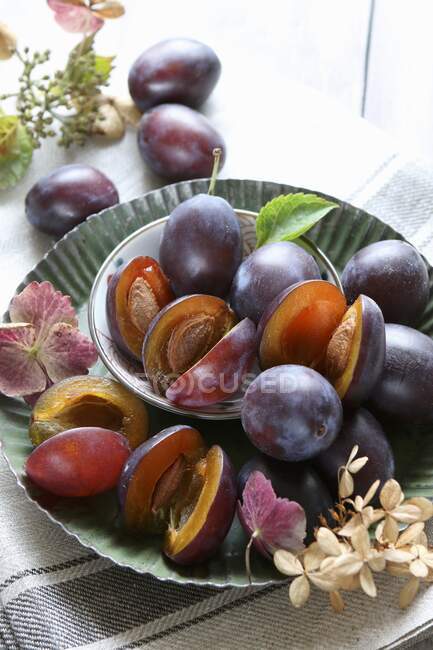 Fresh plums in metal bowls with plants and leaves — Stock Photo