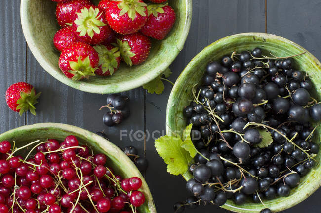Fresh strawberries, redcurrants and blackcurrants in ceramic bowls — Stock Photo