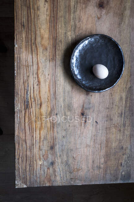 Nur ein Ei auf einem schwarzen Teller am Holztisch — Stockfoto