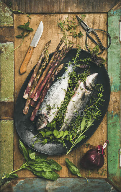 Roher Wolfsbarsch mit Kräutern und Gemüse vor rustikalem Holzhintergrund — Stockfoto