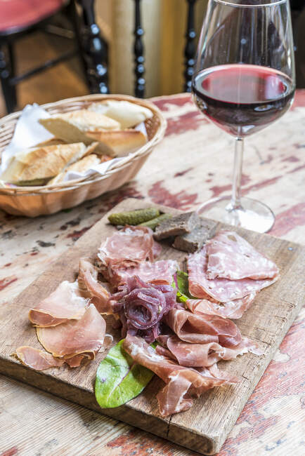 Board with cold meats and charcuteries, salami, prosciutto with bread in the background — Stock Photo