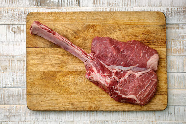 Un steak tomahawk de veau cru sur une planche à découper en bois — Photo de stock
