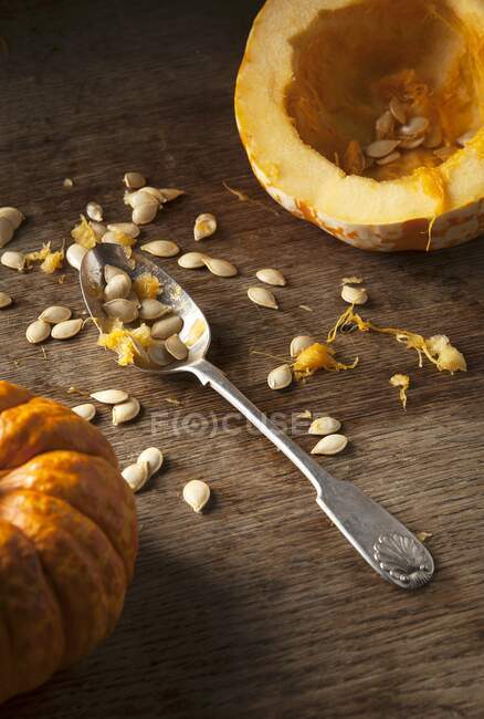 A hollowed out munchkin pumpkin, pumpkin seeds and a vintage spoon on a rustic wooden background — Stock Photo