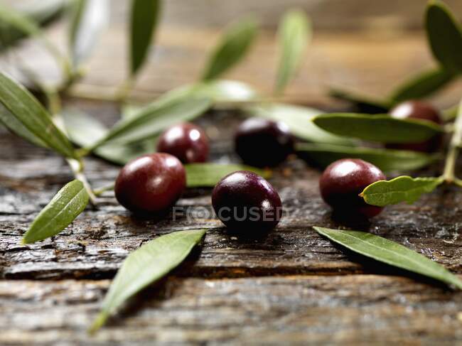 Черные оливки с листьями на деревянной поверхности — стоковое фото