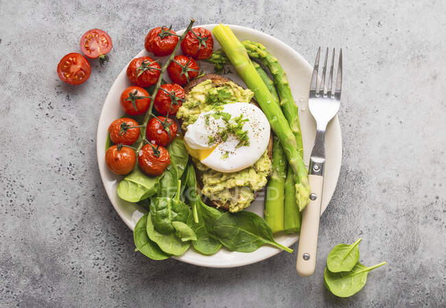 Toast mit Avocadocreme und pochiertem Ei, serviert mit Tomaten, Spinat und Spargel — Stockfoto