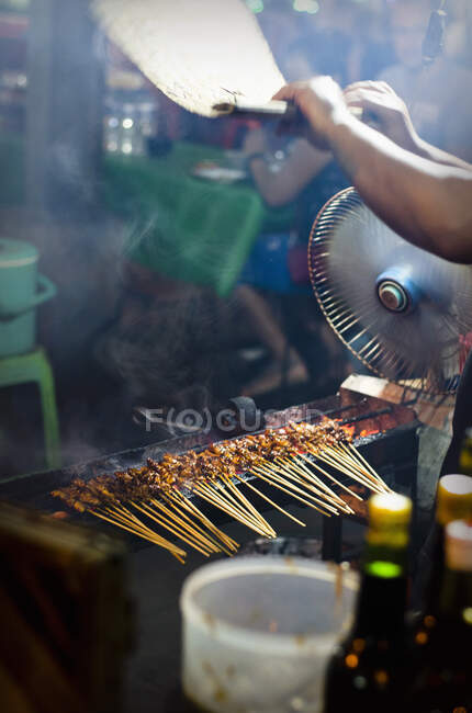 Satay sticks on the grill being fanned at a market in Bali — Stock Photo