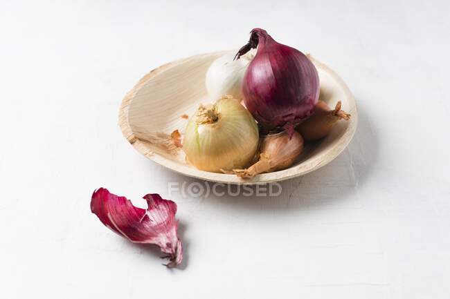 Разнообразный лук на деревянной тарелке — стоковое фото