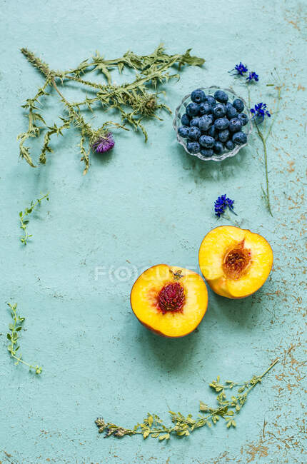 Old blue background with herbarium, blueberries and halved ripe peach — Stock Photo