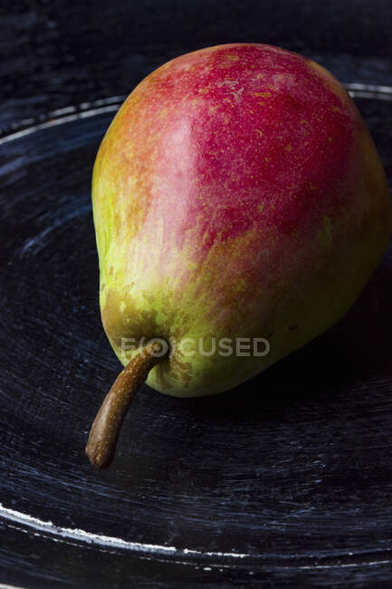 Una pera en una placa de madera negra - foto de stock