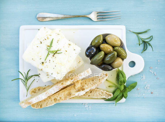 Fresh feta cheese with olives, basil, rosemary and bread slices — Stock Photo