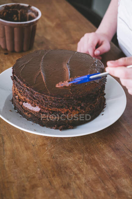 Ребенок делает шоколадный торт за деревянным столом — стоковое фото