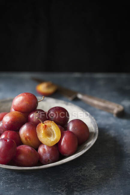 Fresh plums in bowl, one halved and knife on background — Stock Photo