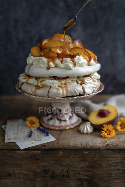 Bolo Pavlova com pêssegos, molho de caramelo e peneiração de açúcar em pó — Fotografia de Stock