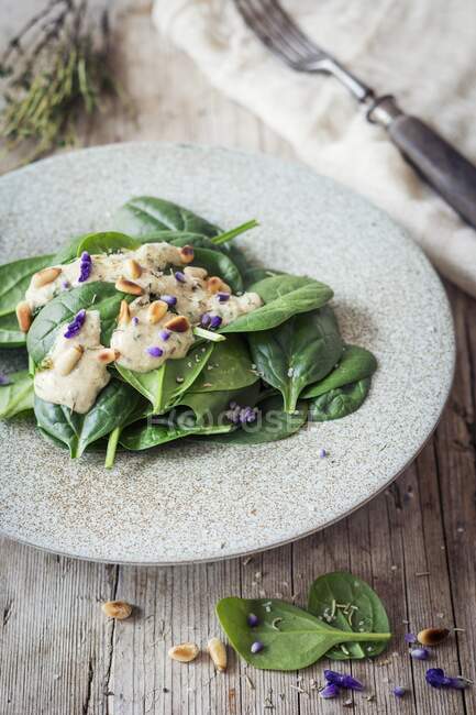 Vegan spinach salad with garlic dressing, pine nuts and edible flowers — Stock Photo