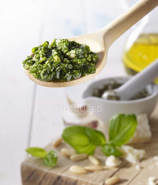 Pesto auf einem Holzlöffel über einem Holzbrett mit Basilikum, Pinienkernen und Olivenöl — Stockfoto