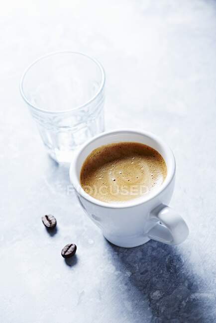 Una tazza di espresso, un bicchiere d'acqua e chicchi di caffè — Foto stock