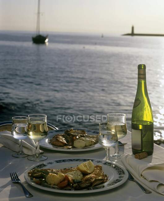 Две тарелки еды и вина на накрытом столе у моря — стоковое фото
