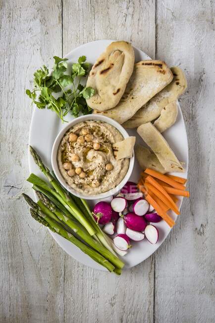 Hummus dip con sésamo, servido con pan plano y verduras crudas - foto de stock