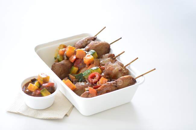 Pork skewers with vegetable sauce in a takeaway box — Stock Photo