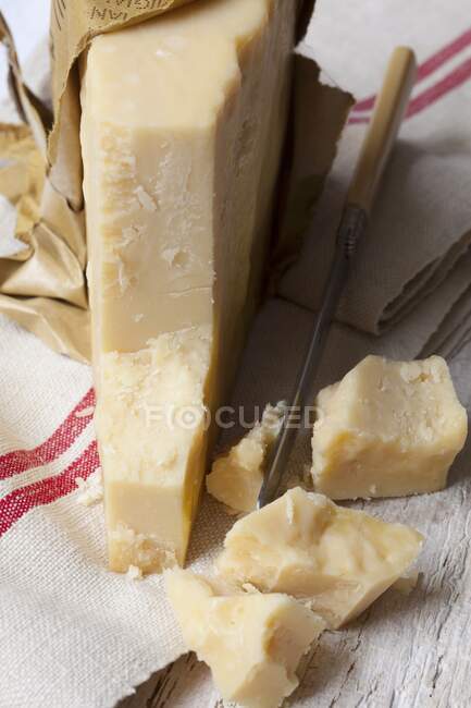 Кусочек сыра пармезан на деревенской ткани с маленьким ножом — стоковое фото